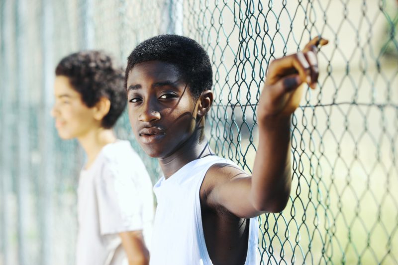 Two boys leaning on a chain-link fence